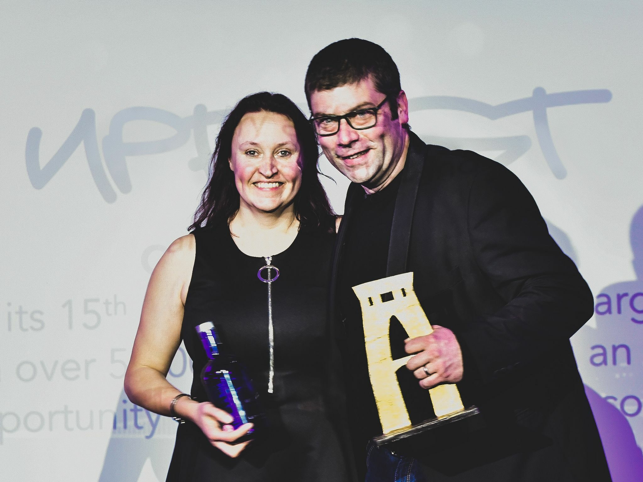 Stephen & Emma Hayles, Founders at Upfest. A couple proudly holding awards, both are wearing black outfits.