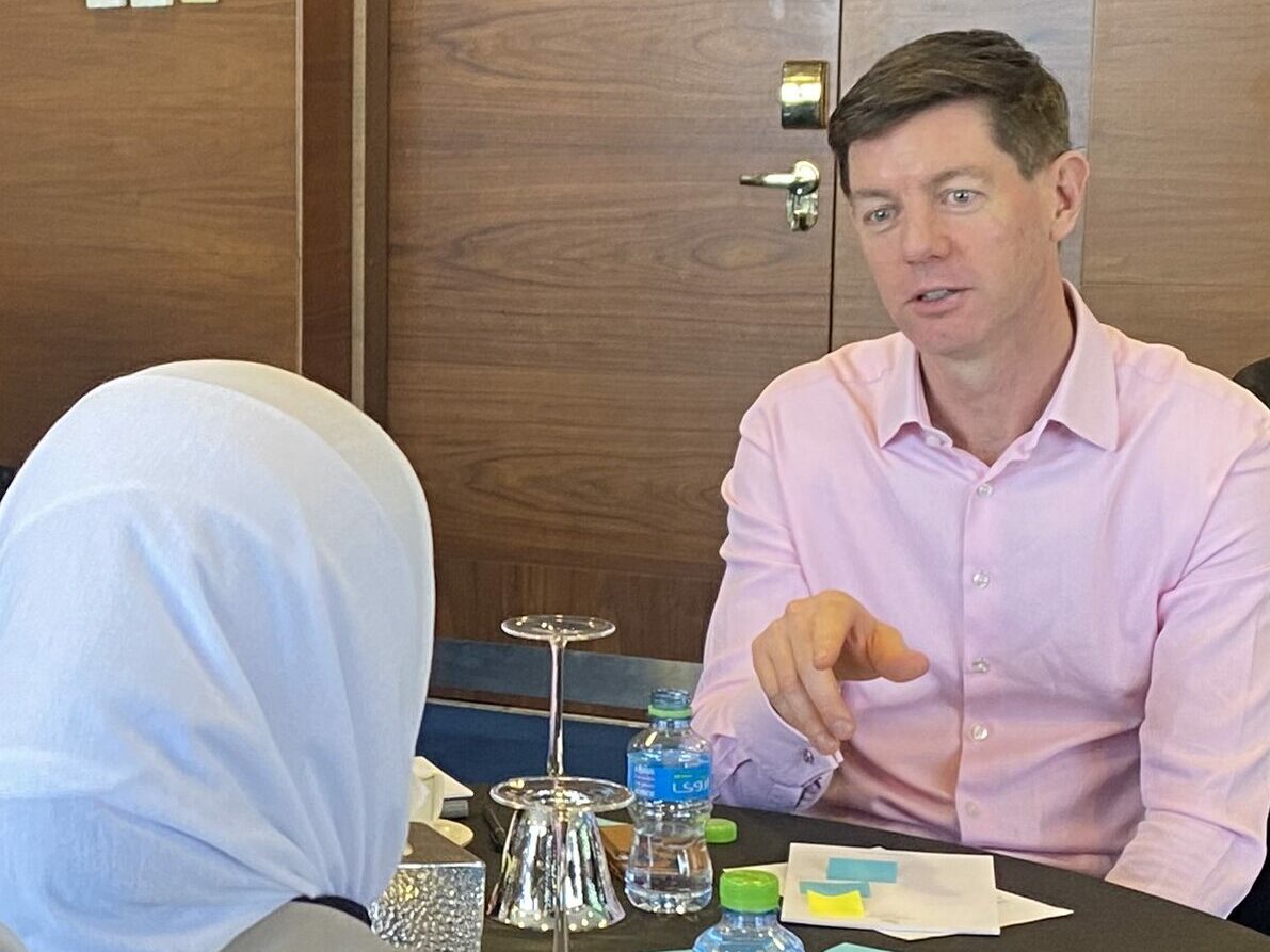 A couple having a discussion over a business table. The man is wearing a pick shirt and the woman has her back to us, she is wearing a white headscarf.