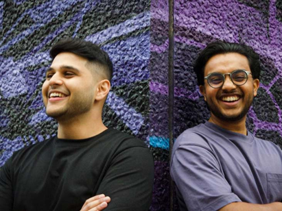 Two men smiling and leaning against a wall having just recieved crowdfunding and investment